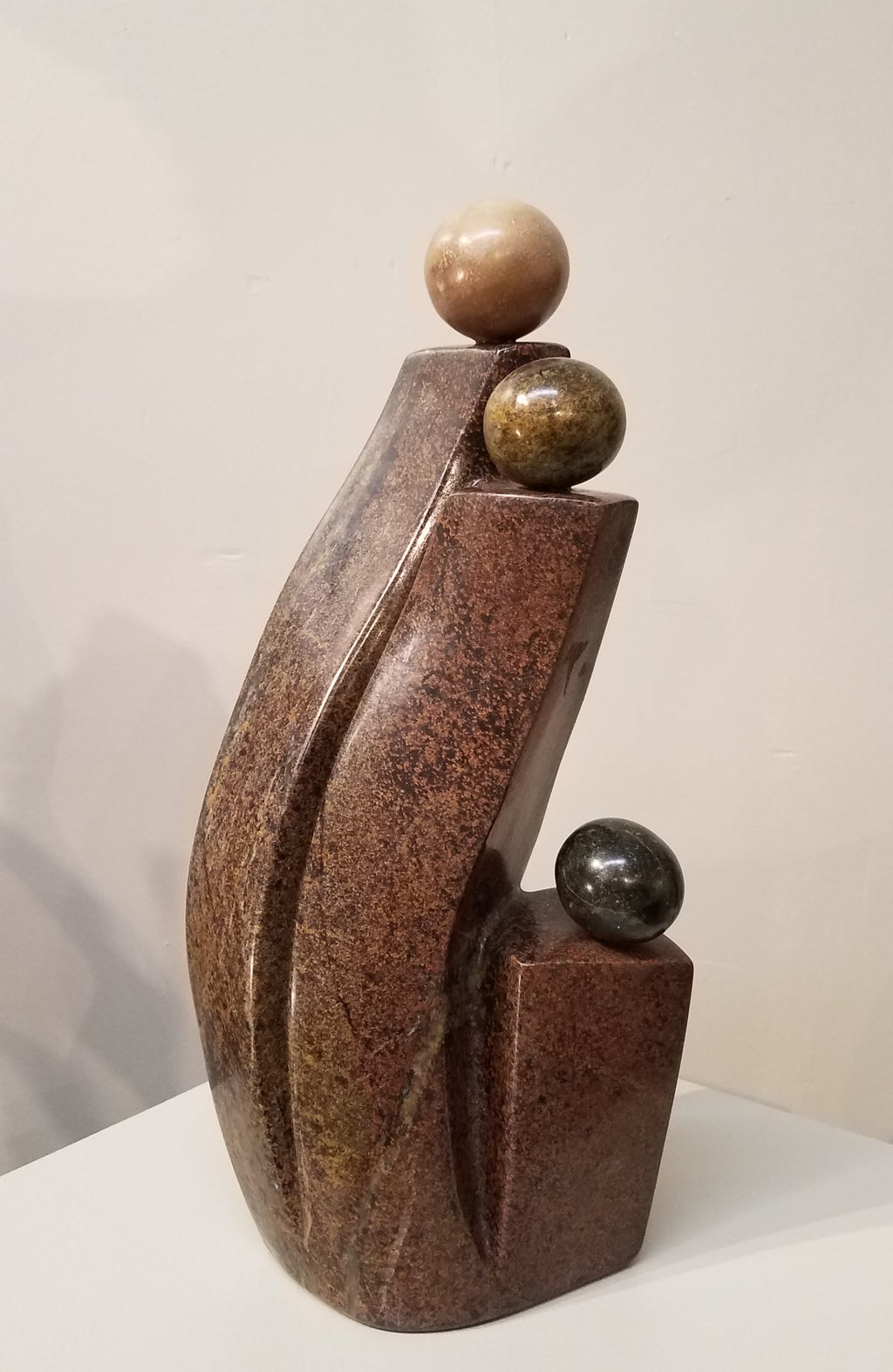 Abstract stone sculpture of a Family, 2 parents with one child. Color Range: Brown, Black. 