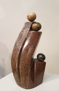 Abstract stone sculpture of a family, two parents with one child. Color Range: Brown, Black.