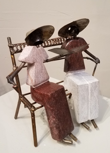 Sculpture of a couple sitting on a bench reading together from the same book. It was created from a combination of rapoko stone (a soft serpentine), and metal, in Zimbabwe. The people’s bodies are sculpted from stone, and the bench, arms, legs, heads and hats, are all metal, welded and soldered together.