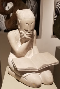 Stone sculpture of a girl reading a book. The stone color is white, with the more sanded and smooth areas being slightly a cream color, or off white. The dimensions are 16.5”H x 10”W x 11.5”D - 60 lbs.