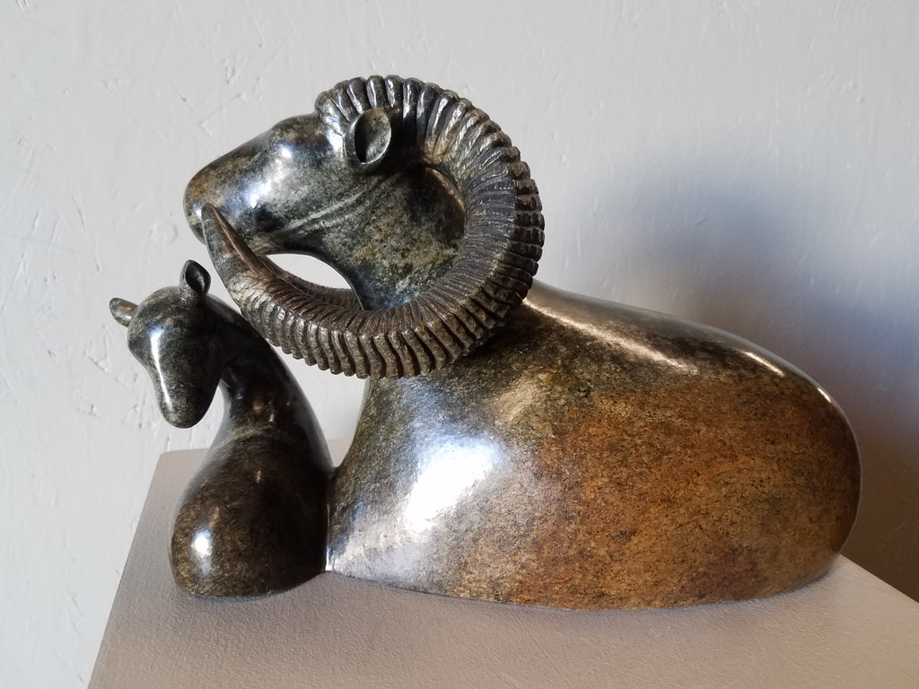 Stone sculpture of a bighorn sheep with a lamb (baby bighorn). The dimensions are 8”H x 12.5”W x 6”D - 15 lbs. The colors of the stone are greenish and rust.