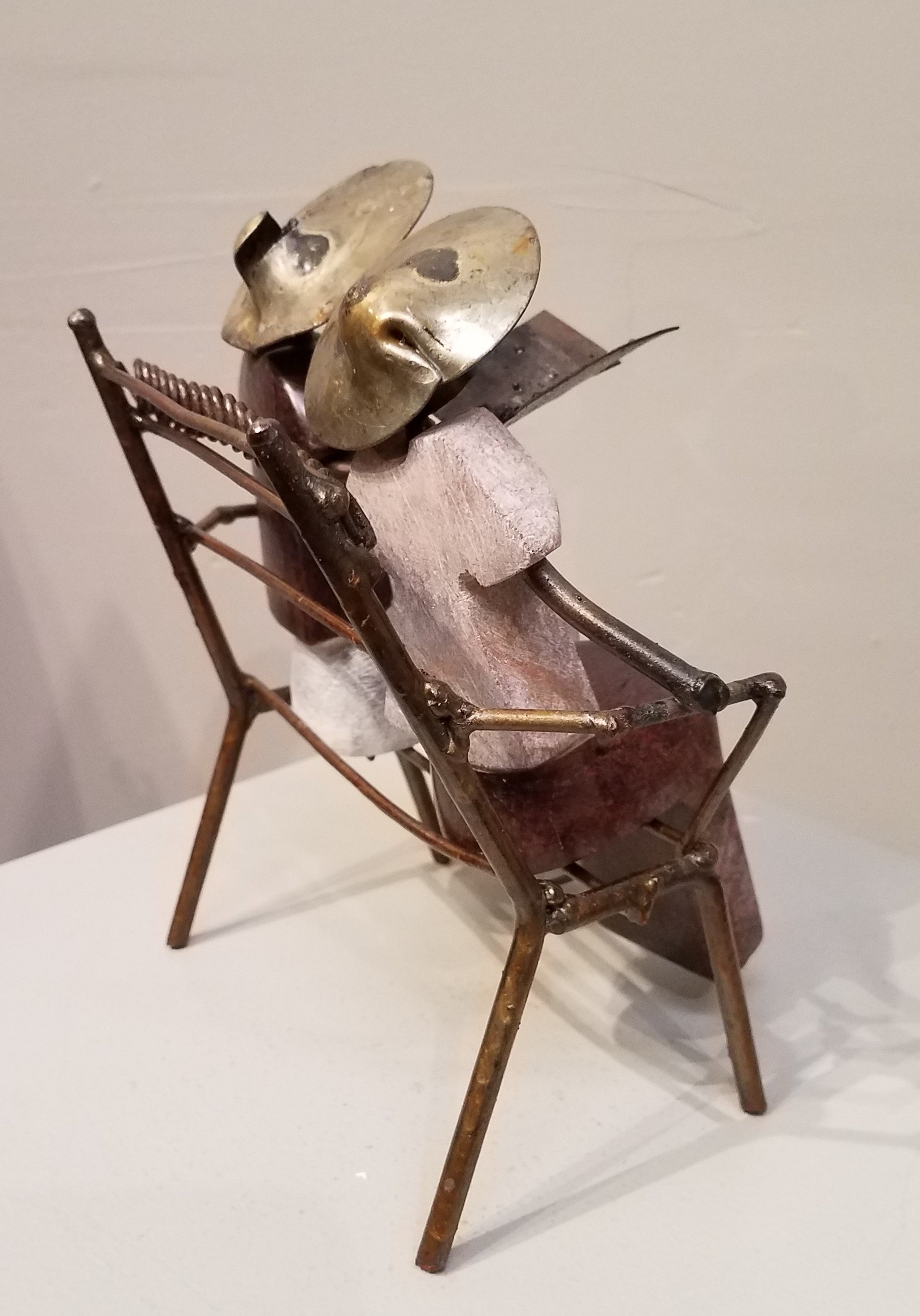 Sculpture of a couple sitting on a bench reading together from the same book. It was created from a combination of rapoko stone (a soft serpentine), and metal, in Zimbabwe. The people’s bodies are sculpted from stone, and the bench, arms, legs, heads and hats, are all metal, welded and soldered together.
