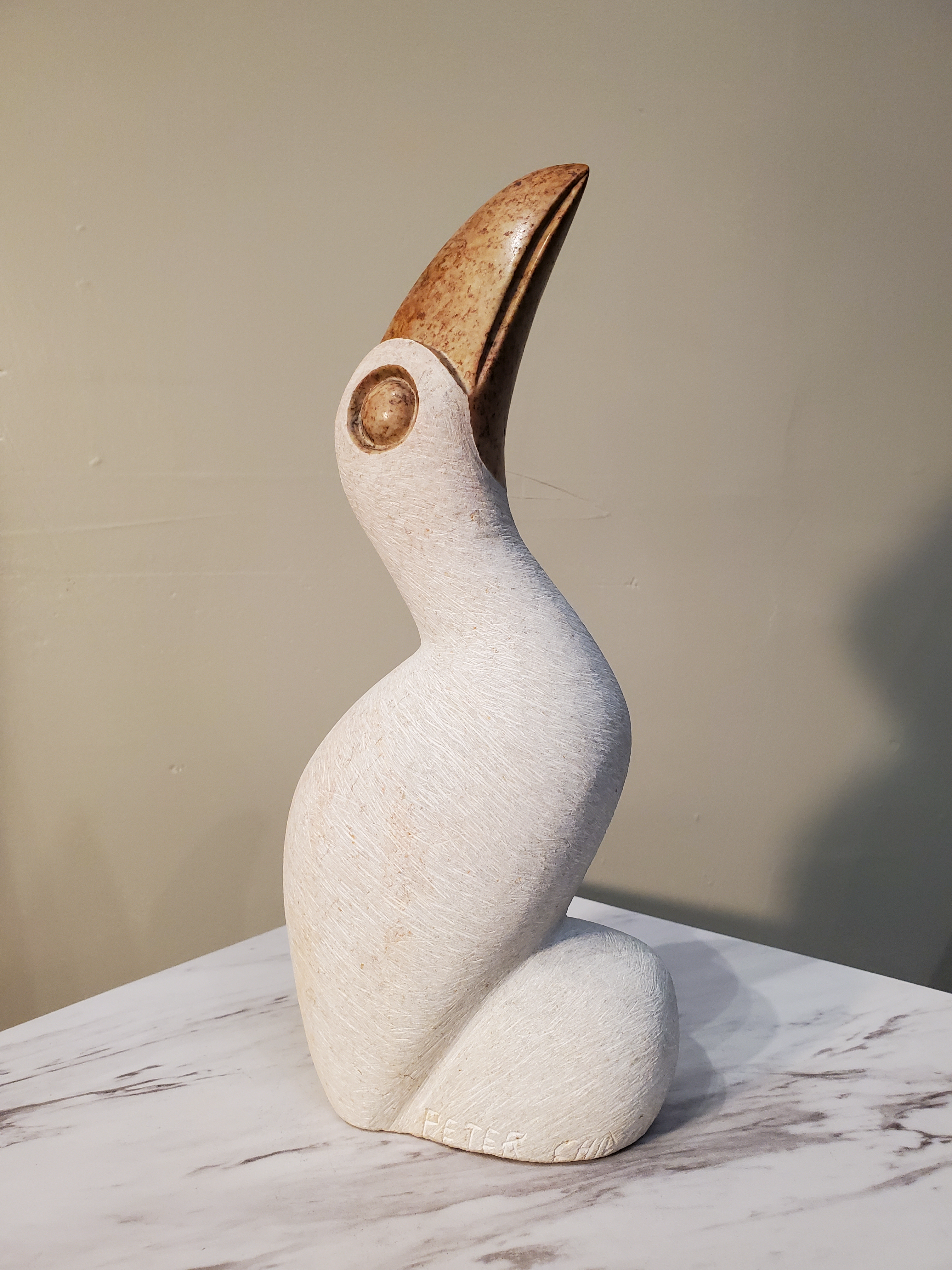 A beautiful perched white pelican looking inquisitively upward. This bird was sculpted from a single piece of opal stone. The white bird is accentuated by a bronze colored beak and eyes. Colors included: White, Bronze.  